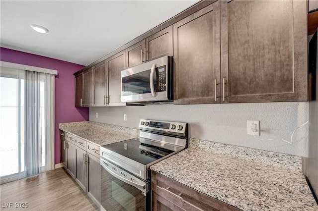 6940 Crescent Gold St, North Las Vegas, NV 89086 - kitchen featuring stainless steel appliances, dark brown cabinetry, light wood-style floors, and light stone counters