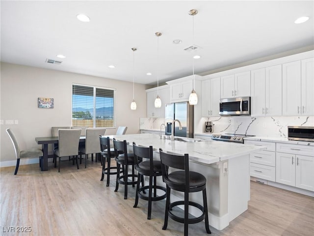 1500 E Laguna St, Pahrump, NV 89048 - kitchen with stainless steel appliances, a kitchen island with sink, decorative backsplash, a kitchen bar, and light wood finished floors