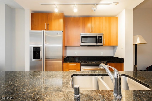200 W Sahara Ave Unit 910, Las Vegas, NV 89102 - kitchen with stainless steel appliances, dark stone counters, a sink, track lighting, and brown cabinets