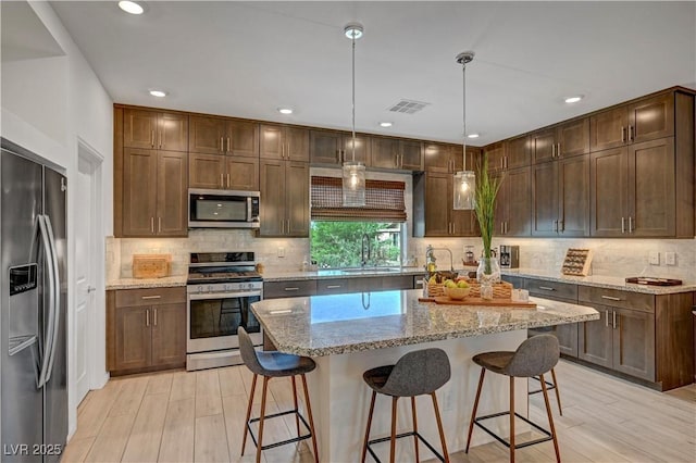 7756 Seville Estates Ct, Las Vegas, NV 89113 - kitchen featuring appliances with stainless steel finishes, light wood-style flooring, a kitchen breakfast bar, tasteful backsplash, and recessed lighting