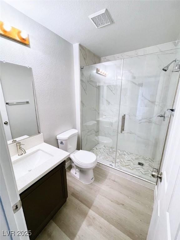 full bath with toilet, vanity, wood finished floors, a marble finish shower, and a textured ceiling