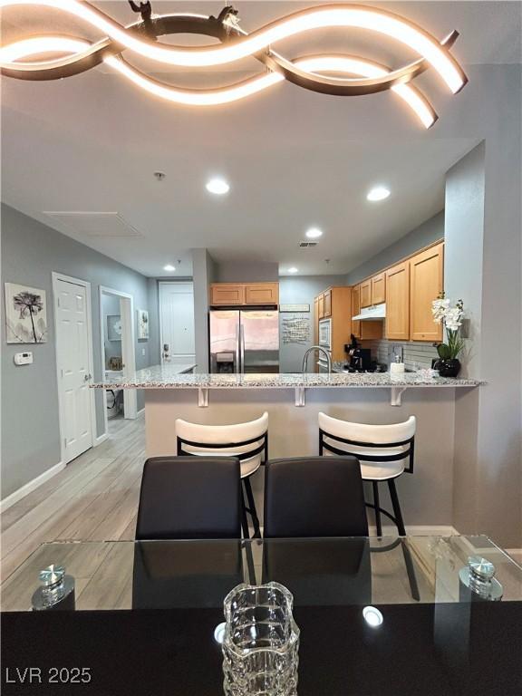 23 E Agate Ave Unit 301, Las Vegas, NV 89123 - kitchen featuring stainless steel fridge with ice dispenser, light brown cabinetry, a peninsula, a kitchen breakfast bar, and tasteful backsplash