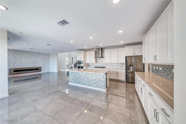 1038 Delbrook Ave, Henderson, NV 89012 - kitchen featuring appliances with stainless steel finishes, wall chimney exhaust hood, backsplash, a large fireplace, and white cabinets