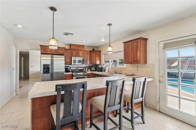 1912 Parkchester Dr, Las Vegas, NV 89108 - kitchen with appliances with stainless steel finishes, tile countertops, decorative backsplash, light tile patterned flooring, and a breakfast bar area