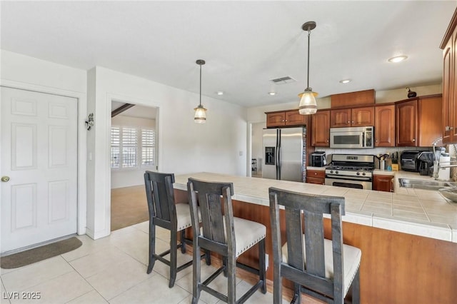 1912 Parkchester Dr, Las Vegas, NV 89108 - kitchen with appliances with stainless steel finishes, a peninsula, a kitchen bar, a sink, and hanging light fixtures