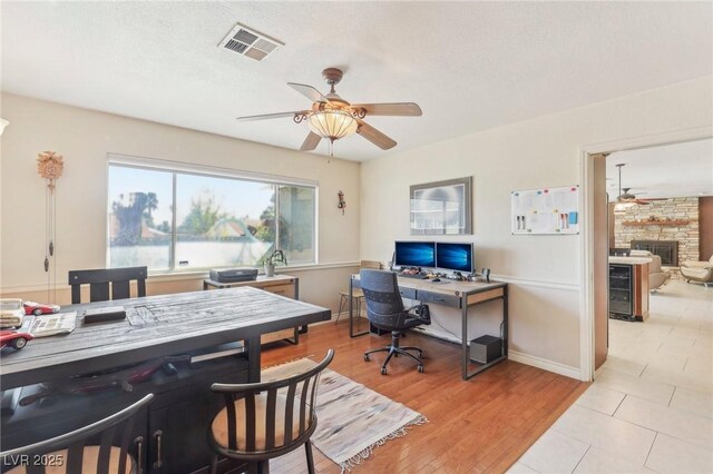 1912 Parkchester Dr, Las Vegas, NV 89108 - office area featuring a ceiling fan, wine cooler, a stone fireplace, light wood-type flooring, and baseboards