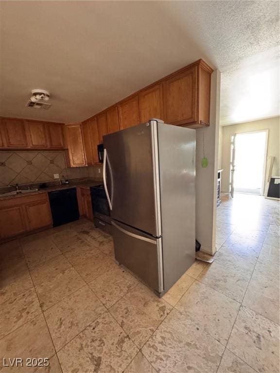 2604 Webster St, North Las Vegas, NV 89030 - kitchen with freestanding refrigerator, black dishwasher, brown cabinets, decorative backsplash, and a textured ceiling