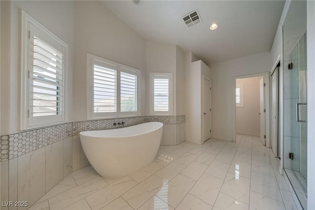 9792 Crescent Lodge Ct, Las Vegas, NV 89178 - bathroom featuring healthy amount of natural light, marble look tile flooring, a freestanding bath, a stall shower, and a wainscoted wall