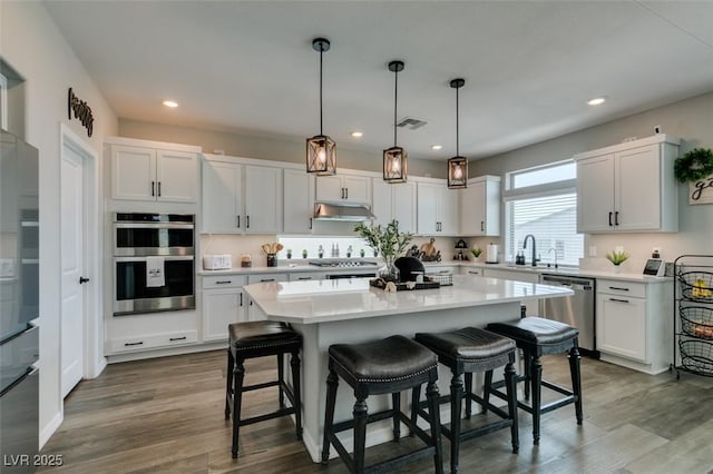 7077 Sunland Hills Ave, Las Vegas, NV 89113 - kitchen with appliances with stainless steel finishes, a kitchen breakfast bar, under cabinet range hood, light countertops, and recessed lighting