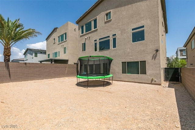 7077 Sunland Hills Ave, Las Vegas, NV 89113 - rear view of property featuring a trampoline, stucco siding, and a fenced backyard