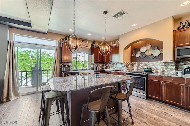 8121 Russell Creek Ct, Las Vegas, NV 89139 - kitchen with appliances with stainless steel finishes, a breakfast bar area, stone counters, a kitchen island, and decorative backsplash
