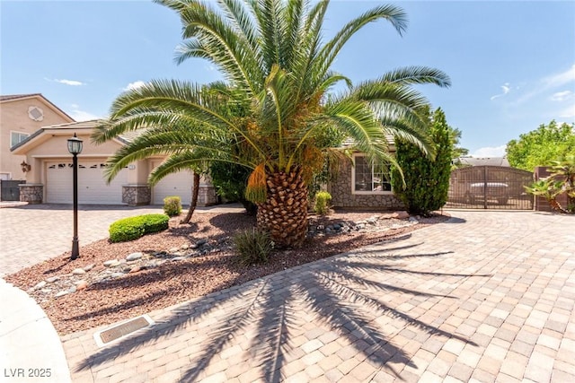 6779 Rainstorm Ridge Ave, Las Vegas, NV 89131 - view of property hidden behind natural elements with decorative driveway, stone siding, a garage, a gate, and stucco siding