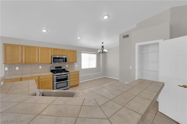 3228 Jumping Hills Ave, Henderson, NV 89052 - kitchen with appliances with stainless steel finishes, tile countertops, a chandelier, baseboards, and decorative backsplash