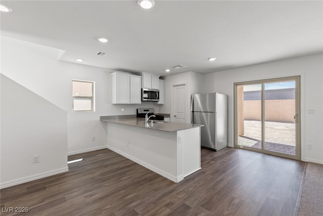 6252 Blood Lily Ave, Las Vegas, NV 89122 - kitchen with stainless steel appliances, a peninsula, white cabinets, dark wood-style floors, and baseboards