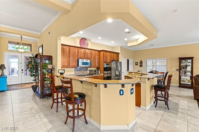5940 Vizzi Ct, Las Vegas, NV 89131 - kitchen featuring stainless steel appliances, a breakfast bar area, crown molding, light stone counters, and brown cabinets