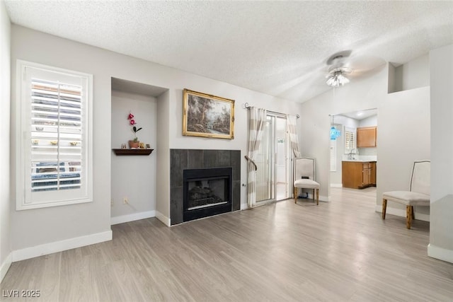 3157 Capetown Way, Las Vegas, NV 89128 - living area featuring a textured ceiling, light wood-style flooring, baseboards, a tile fireplace, and vaulted ceiling