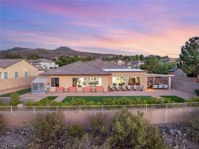 20 Kittansett Loop, Henderson, NV 89052 - back of house at dusk with outdoor lounge area, a mountain view, a fenced backyard, stucco siding, and a patio