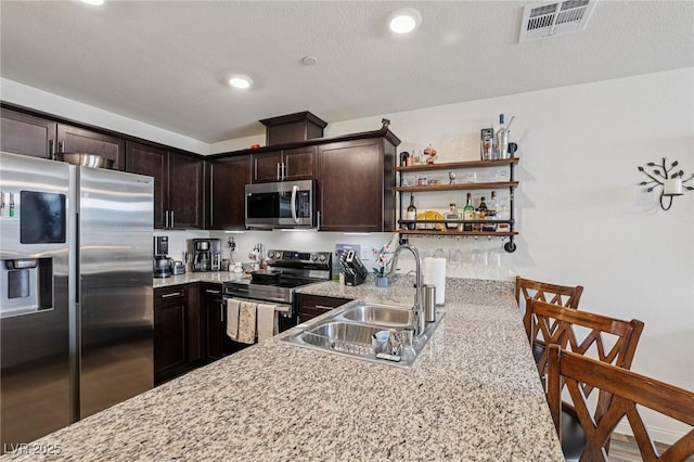 6807 Satin Silver Ct, North Las Vegas, NV 89086 - kitchen featuring appliances with stainless steel finishes, a sink, dark brown cabinetry, open shelves, and light stone countertops