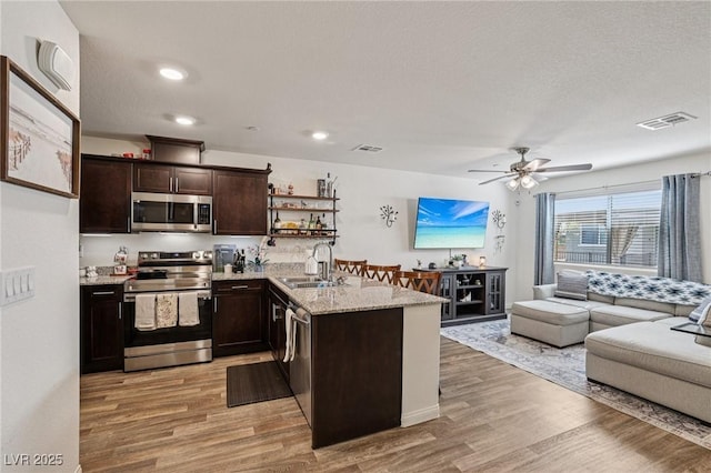 6807 Satin Silver Ct, North Las Vegas, NV 89086 - kitchen featuring appliances with stainless steel finishes, a sink, light wood-style floors, dark brown cabinets, and open floor plan