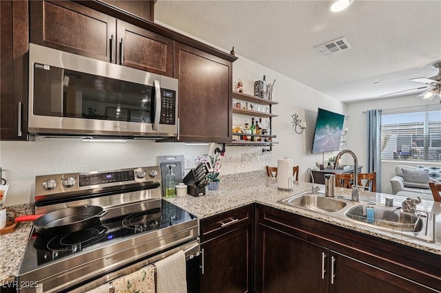 6807 Satin Silver Ct, North Las Vegas, NV 89086 - kitchen with stainless steel appliances, a sink, dark brown cabinetry, open shelves, and light stone counters
