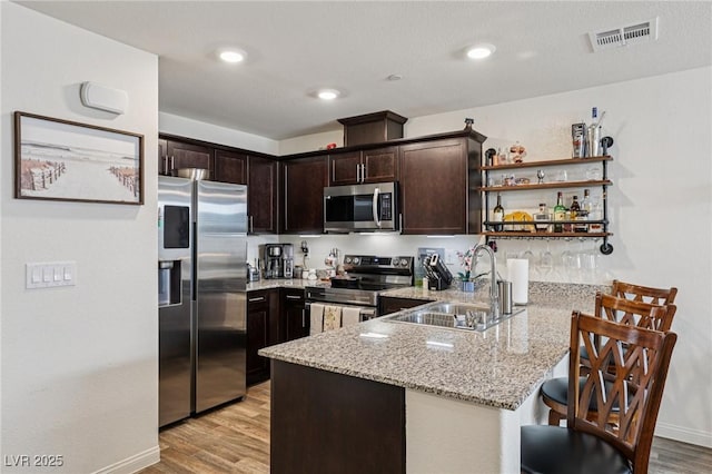 6807 Satin Silver Ct, North Las Vegas, NV 89086 - kitchen featuring appliances with stainless steel finishes, a sink, a peninsula, dark brown cabinetry, and light stone countertops
