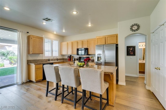 2418 Brockton Way, Henderson, NV 89074 - kitchen with black microwave, stainless steel fridge with ice dispenser, light brown cabinetry, dishwasher, and a kitchen bar