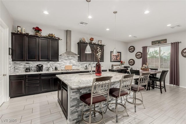 5616 Silver Cascade Ave, Las Vegas, NV 89131 - kitchen featuring wall chimney exhaust hood, tasteful backsplash, a breakfast bar area, light stone countertops, and a sink