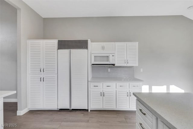 5008 Shoal Creek Cir, Las Vegas, NV 89113 - kitchen with built in refrigerator, white microwave, white cabinets, light wood-type flooring, and baseboards