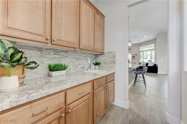 2168 Big Bar Dr, Henderson, NV 89052 - kitchen with a sink, light wood-style flooring, backsplash, light stone counters, and baseboards