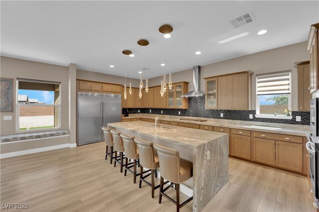 7258 W Le Baron Ave, Las Vegas, NV 89178 - kitchen with stainless steel appliances, wall chimney range hood, a kitchen island with sink, a breakfast bar area, and backsplash