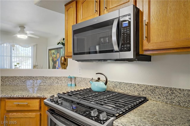 698 S Racetrack Rd Unit 1714, Henderson, NV 89015 - kitchen featuring appliances with stainless steel finishes, a ceiling fan, light stone countertops, and brown cabinetry