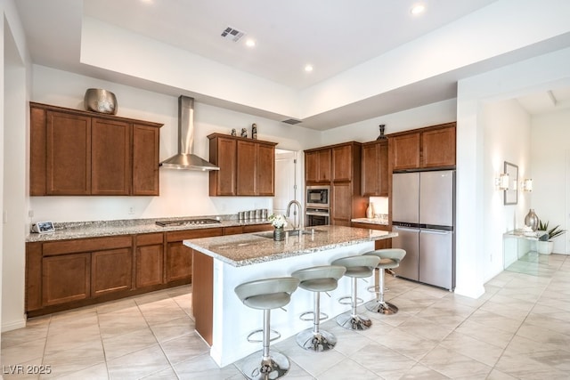 6728 Regency Ridge Ct, Las Vegas, NV 89148 - kitchen featuring appliances with stainless steel finishes, wall chimney exhaust hood, a sink, a kitchen island with sink, and light stone countertops