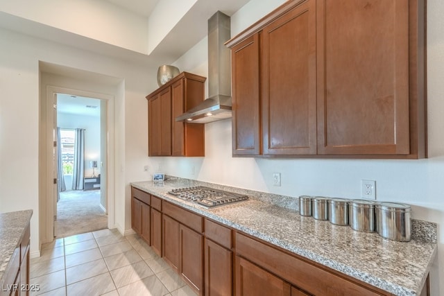 6728 Regency Ridge Ct, Las Vegas, NV 89148 - kitchen with wall chimney exhaust hood, stainless steel gas stovetop, brown cabinets, light colored carpet, and light stone countertops