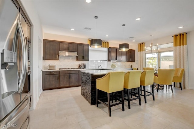 7208 Grace Estate Ave, Las Vegas, NV 89113 - kitchen with stainless steel fridge, under cabinet range hood, dark brown cabinets, a kitchen island, and backsplash