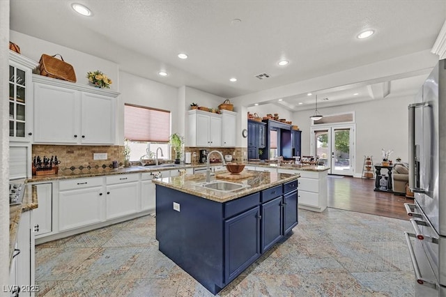 7408 Via Fiorentino St, Las Vegas, NV 89131 - kitchen with blue cabinets, white cabinetry, a peninsula, an island with sink, and tasteful backsplash