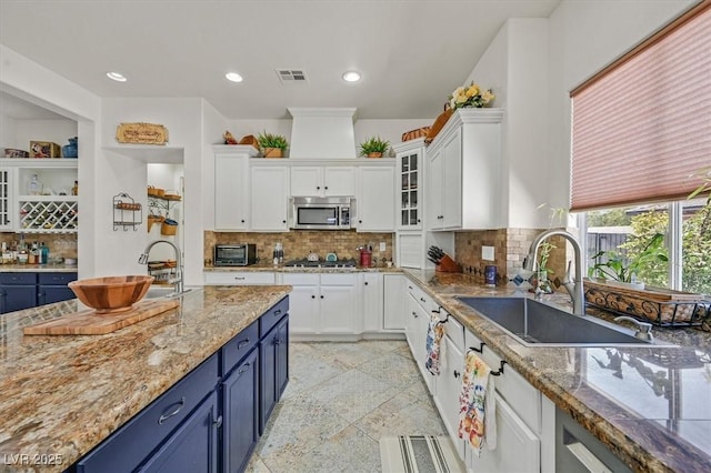 7408 Via Fiorentino St, Las Vegas, NV 89131 - kitchen featuring blue cabinetry, stainless steel appliances, white cabinets, backsplash, and light stone countertops