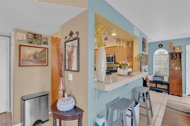 7950 W Flamingo Rd Unit 1003, Las Vegas, NV 89147 - kitchen with range, stainless steel microwave, a kitchen bar, light tile patterned floors, and light countertops