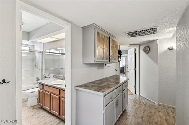 3201 Beacon Shores Cir, Las Vegas, NV 89117 - kitchen with light wood-type flooring, a sink, gray cabinets, a textured ceiling, and a textured wall
