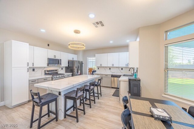 747 Canyon Crest Dr, Las Vegas, NV 89123 - kitchen with stainless steel appliances, light wood-type flooring, a kitchen bar, a kitchen island, and backsplash