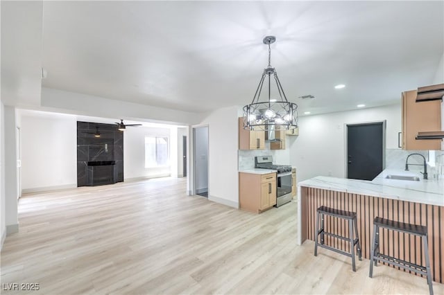 1805 Amboy Dr, Las Vegas, NV 89108 - kitchen featuring stainless steel range with gas stovetop, tasteful backsplash, light wood-style floors, a kitchen bar, and a premium fireplace