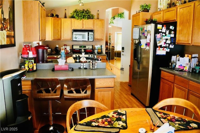 9355 W Viking Rd, Las Vegas, NV 89147 - kitchen featuring appliances with stainless steel finishes, light wood-style flooring, a peninsula, arched walkways, and a kitchen breakfast bar