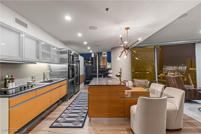 3726 Las Vegas Blvd Unit 606, Las Vegas, NV 89158 - kitchen featuring a sink, black electric cooktop, light wood finished floors, dark countertops, and glass insert cabinets