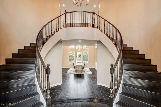 10671 Capesthorne Way, Las Vegas, NV 89135 - stairway featuring a chandelier, baseboards, hardwood / wood-style floors, a towering ceiling, and arched walkways