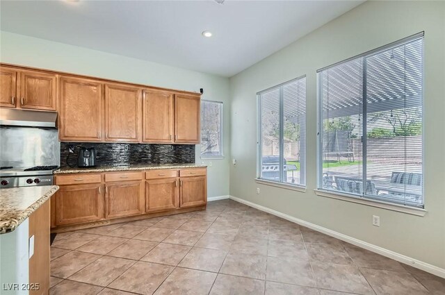313 Glenridding St, Las Vegas, NV 89183 - kitchen featuring under cabinet range hood, tasteful backsplash, light stone countertops, light tile patterned floors, and brown cabinetry