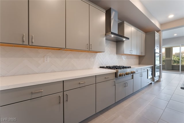 128 Los Cabos Dr Unit 301, Las Vegas, NV 89144 - kitchen featuring wall chimney range hood, gray cabinets, stainless steel appliances, decorative backsplash, and light stone counters
