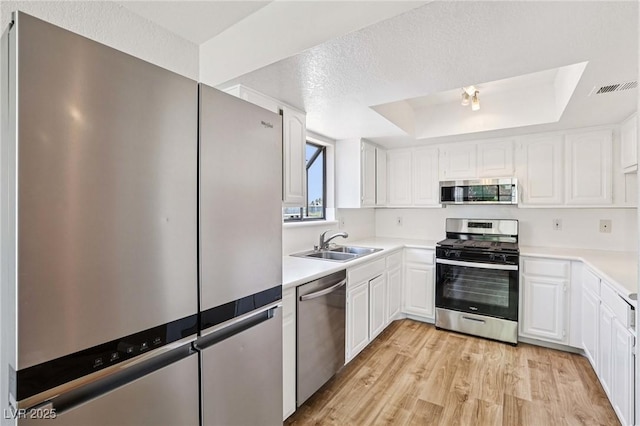 5063 Eldora Ave Unit 4, Las Vegas, NV 89146 - kitchen with appliances with stainless steel finishes, a tray ceiling, a sink, light wood-type flooring, and white cabinetry