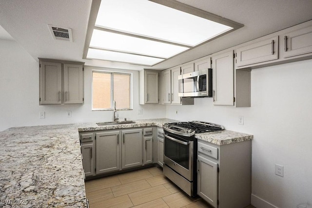 2316 Pine Bluff Ct, Las Vegas, NV 89134 - kitchen with stainless steel appliances, a sink, gray cabinetry, light stone countertops, and light wood-style floors
