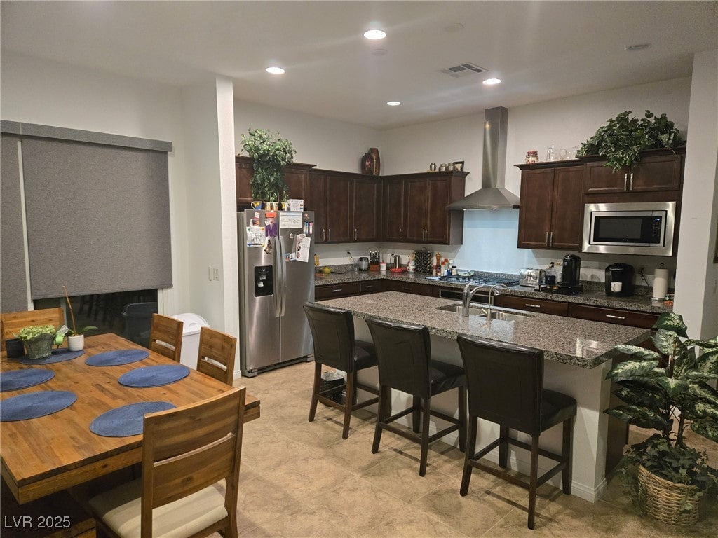 4719 N Transcendental St, North Las Vegas, NV 89031 - kitchen featuring stainless steel appliances, wall chimney exhaust hood, a sink, dark brown cabinets, and an island with sink