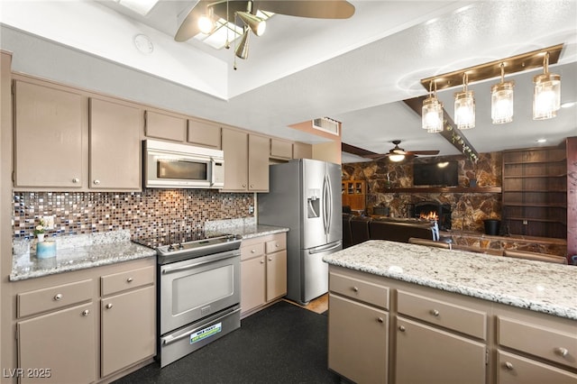 6612 Elton Ave, Las Vegas, NV 89107 - kitchen featuring a ceiling fan, appliances with stainless steel finishes, decorative backsplash, cream cabinetry, and a stone fireplace