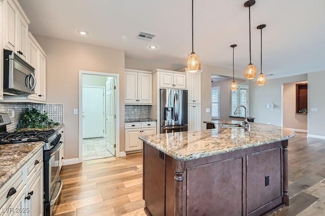 4311 Fiore Bella Blvd, Las Vegas, NV 89135 - kitchen with stainless steel appliances, light wood-type flooring, tasteful backsplash, a kitchen island with sink, and light stone countertops